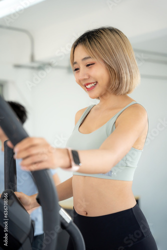 Asian woman exercising with elliptical walking machine at gym. She training at walking machine. Woman walking on gym machine with smile.