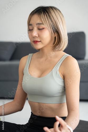 Beautiful young asian woman doing yoga at her home. Place hands on lap, fingers folded, eyes closed, and meditate. Doing yoga at home. Anxiety reduction concept.