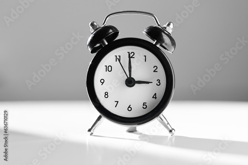 Modern black and white alarm clock in retro style isolated on white and grey background with shadow showing time three hours in afternoon. Siesta time, break, lunch concept.