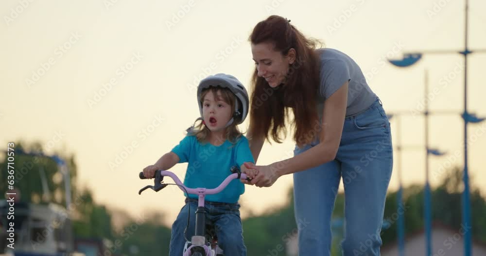 Mom teaches daughter to ride a bike. Happy family childhood dream concept. Mother and little daughter learn to ride a bike in the park. Happy family goes in for sports outdoors sunlight