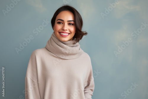 Portrait of a beautiful young woman in sweater and scarf against blue background