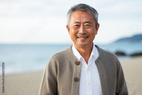 Medium shot portrait of a Chinese man in his 50s in a beach background wearing a chic cardigan
