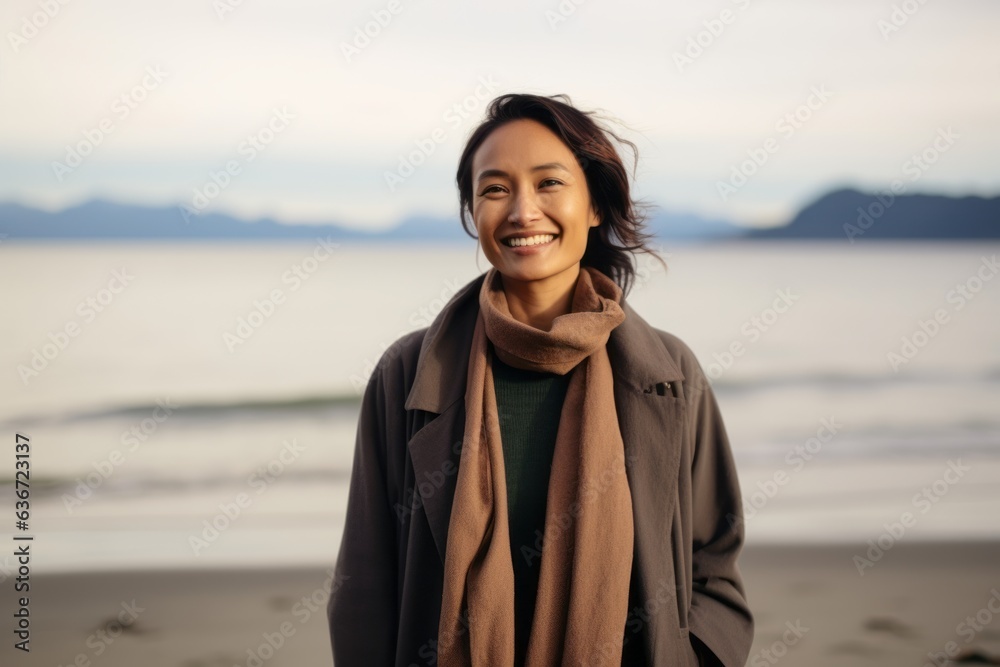 Medium shot portrait of a Indonesian woman in her 30s in a beach background wearing a versatile overcoat Medium shot portrait of a Indonesian woman in her 30s in a beach background wearing a versatile overcoat