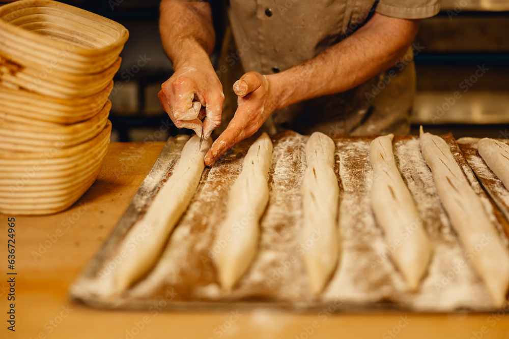 baker cuts top of unbaked baguettes with bread lame before they go in the oven in professional bakery