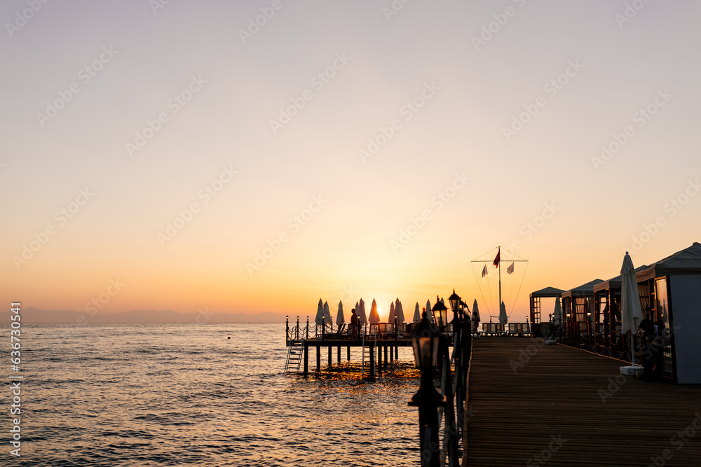 Beautiful sunrise in the Mediterranean Sea, Antalya, Türkiye. Picturesque sunset in Kemer, Turkey. The sun rises over the ocean and the pier with sun umbrellas on the right side