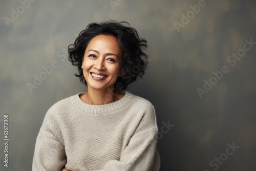 Portrait of a happy young woman standing with arms crossed against grey background © Leon Waltz