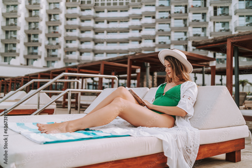 Chica joven en traje de baño leyendo libro en cama balinesa en piscina de hotel de lujo