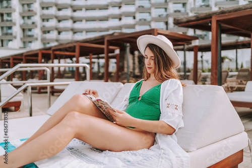 Chica joven en traje de baño leyendo libro en cama balinesa en piscina de hotel de lujo photo