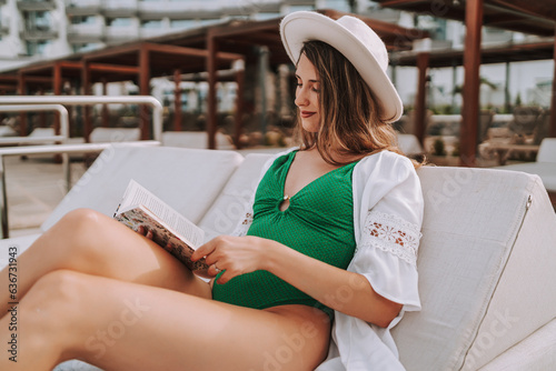 Chica joven en traje de baño leyendo libro en cama balinesa en piscina de hotel de lujo photo