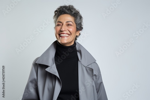 Portrait of smiling middle aged woman in trench coat on grey background