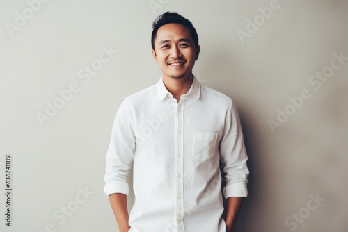 Portrait of handsome young Asian man in white shirt standing against white wall.