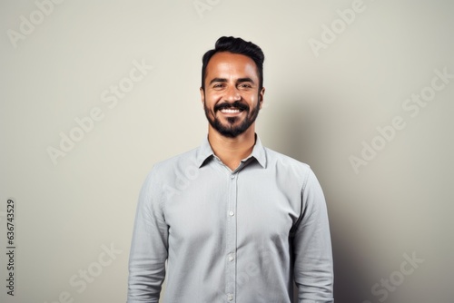 Portrait of a happy young bearded Indian man smiling against grey background