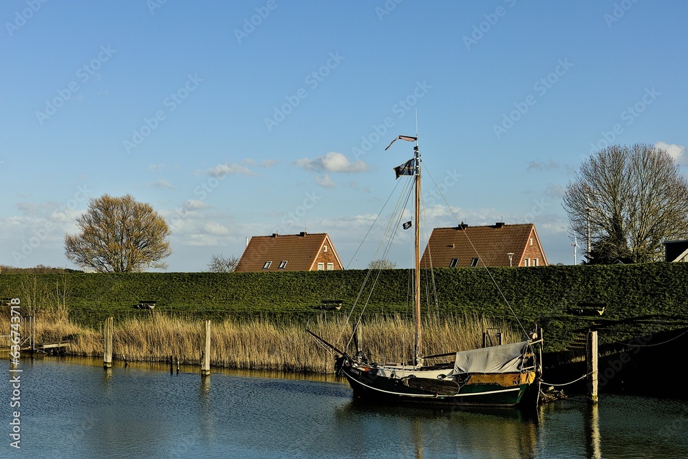 Naklejka premium Scenic view of a small boat docked along the bank of a canal. Hooksiel, Germany, North Sea.