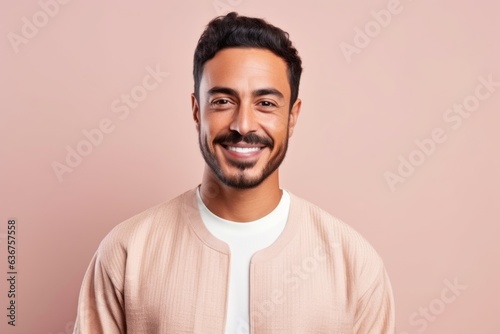 Medium shot portrait of a Saudi Arabian man in his 30s in a pastel or soft colors background wearing a chic cardigan © Hanne Bauer