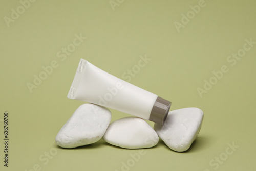 White blank cream tube and pebbles on green background. Template for design, mockup. Beauty concept