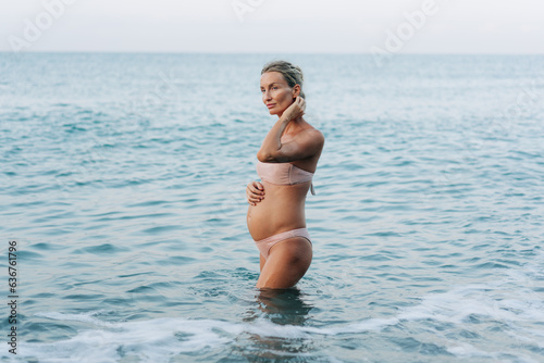 A beautiful pregnant woman enters the sea to freshen up and swim.