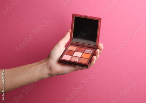 Makeup palette of eye shadows in a female hand on a pink background