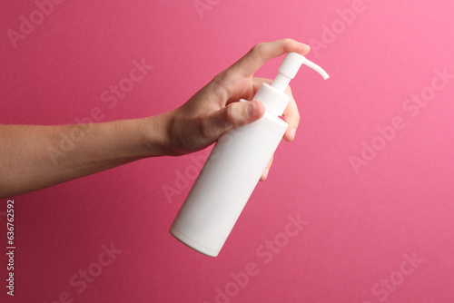 White cream or soap bottle with dispenser in female hand on pink background