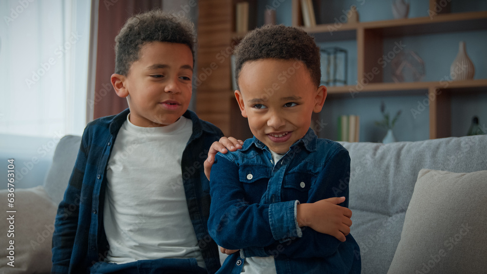 African American boy brother kid sorry apologize make peace after quarrel conflict touching for shoulder upset sad little frustrated child schoolboy pretend offended sit turn back to sibling smiling