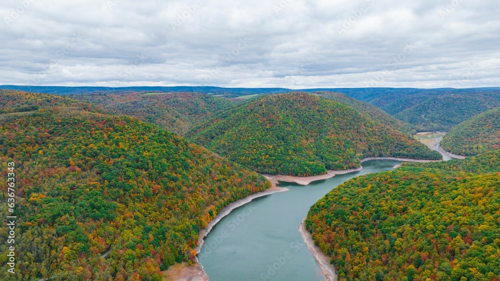 Aerial of a scenic lake surrounded by a dense forest with autumn foliage in fall colors