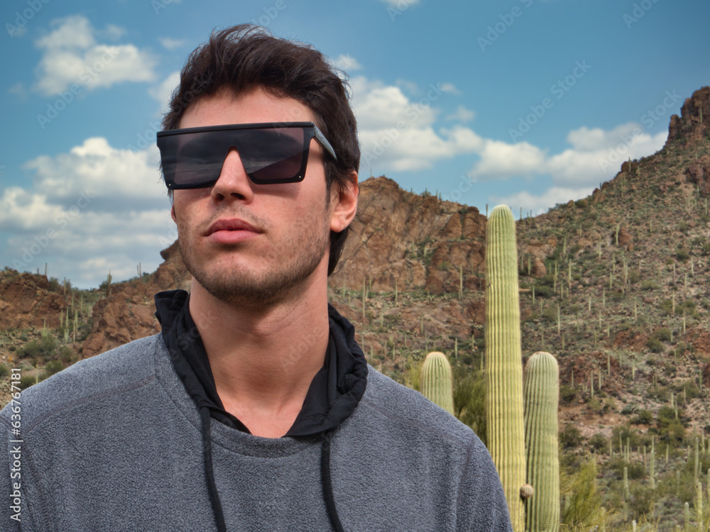 Photo of a stylish man posing in front of a tall cactus wearing sunglasses Photo of a stylish man posing in front of a tall cactus wearing sunglasses