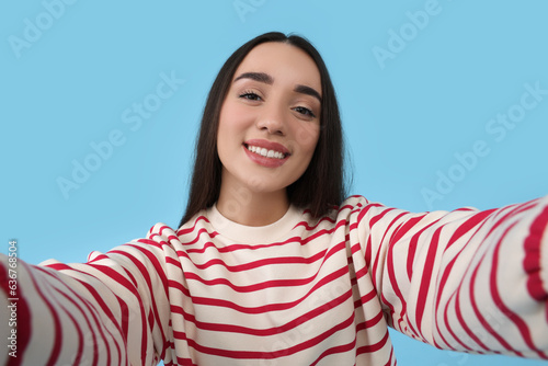 Smiling young woman taking selfie on light blue background