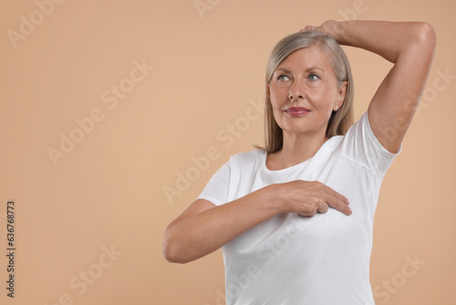 Beautiful senior woman doing breast self-examination on light brown background. Space for text photo
