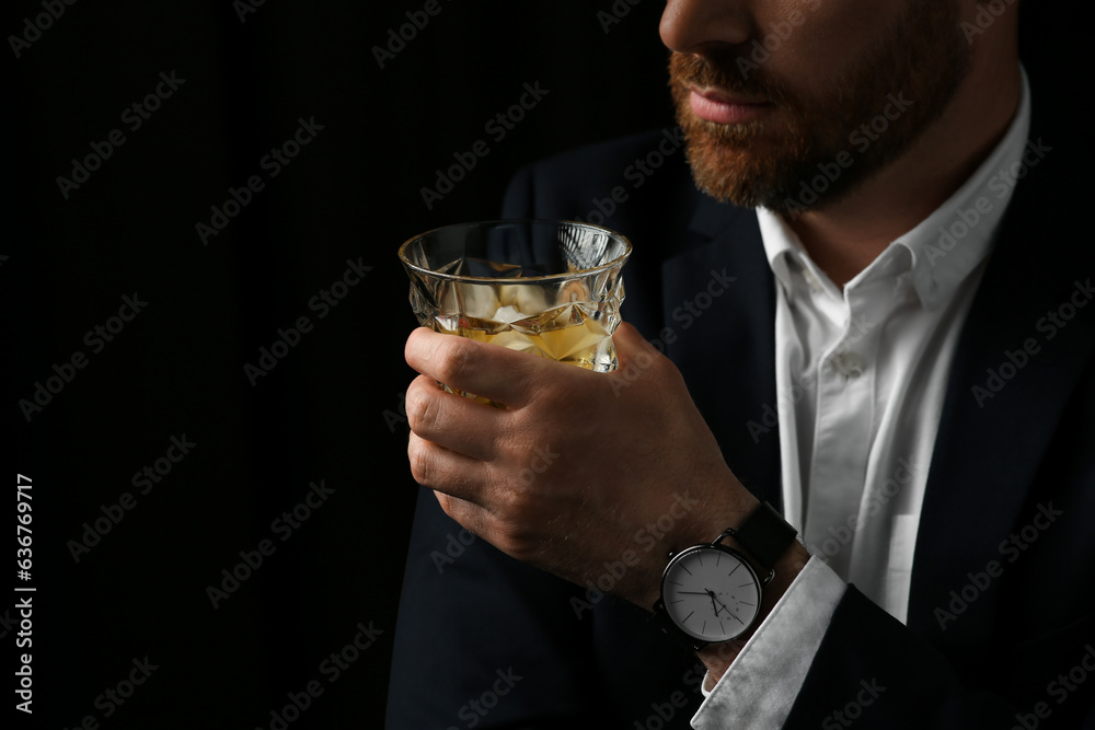 Man holding glass of whiskey with ice cubes on black background, closeup. Space for text