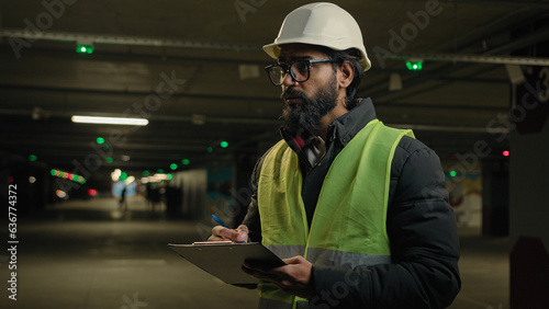 Fotografi Indian contractor mechanic in helmet and glasses writing in paper examination parking lot write in clipboard
