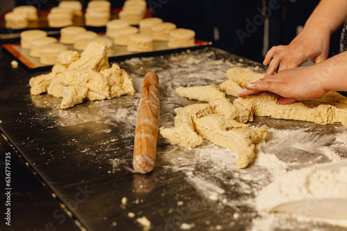 Baker shapes dough on professional metal table in bakery kitchen