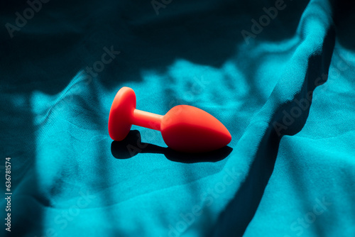 Red silicone anal plug, sex toy, on a blue background in the shade. Contrast photo of anal toys, erotic toys