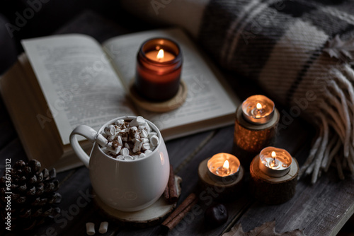 Aromatherapy on a grey fall morning, atmosphere of cosiness and relax. Autumn cozy home composition with hot chocolate with marshmallow and candles. Wooden background, books, close up.