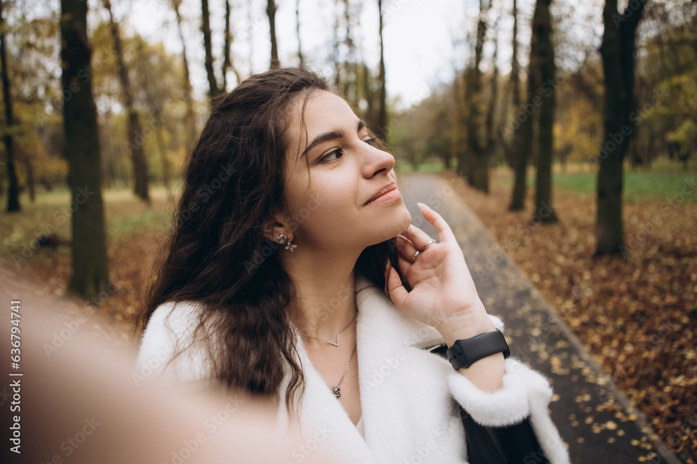 Attractive pretty woman make selfie outdoor, portrait of young lady in warm sunny autumn park season, fall, yellow orange red leaves, dressed leather wool fur jacket smiling having fun Attractive pretty woman make selfie outdoor, portrait of young lady in warm sunny autumn park season, fall, yellow orange red leaves, dressed leather wool fur jacket smiling having fun