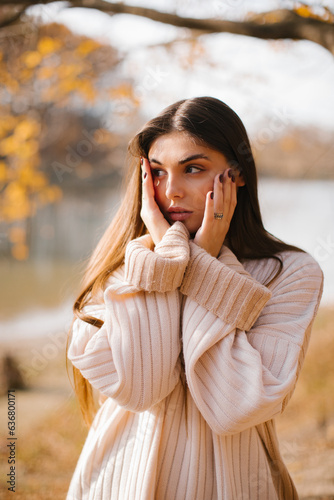Young woman with long hair in a beige sweater in the forest in autumn. Autumn portrait of a woman.
