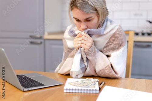 A woman freezes working at home at a music book, reads money. Small salary, debts, loans, taxes, no heat, cold at home. A woman dressed warmly at home in the kitchen works.