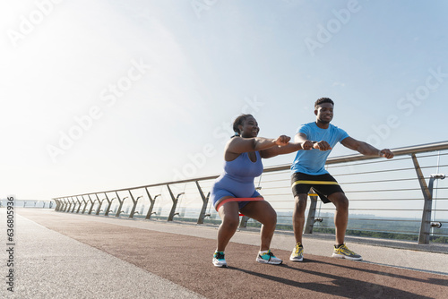 Attractive african american man and woman working out together squatting with fitness bands outdoors