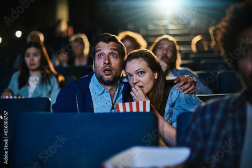 Young couple watching a scary horror movie in a movie theater photo