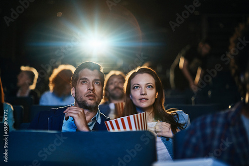 Young couple watching a movie and eating popcorn in a movie theater