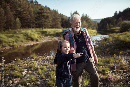 Grandfather and granddaughter hiking by a creek in the forest