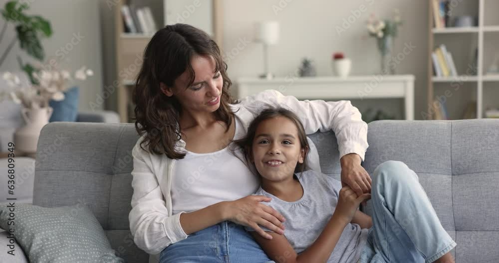 Happy young mom talking to positive preschool daughter with trust, resting with child on sofa, hugging, listening to speaking girl, smiling, laughing, enjoying motherhood, leisure at home Happy young mom talking to positive preschool daughter with trust, resting with child on sofa, hugging, listening to speaking girl, smiling, laughing, enjoying motherhood, leisure at home