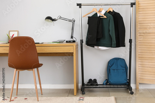Interior of stylish room with modern workplace and school uniform on rack © Pixel-Shot