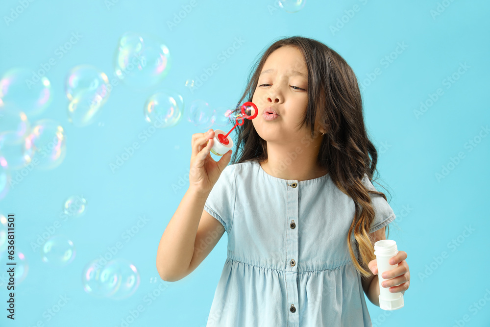 Cute little girl blowing soap bubbles on light blue background Cute little girl blowing soap bubbles on light blue background