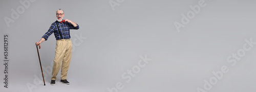 Cheerful senior man with walking cane on gray background. Banner design with space for text