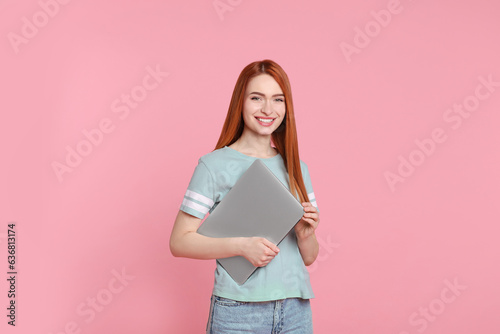 Smiling young woman with laptop on pink background