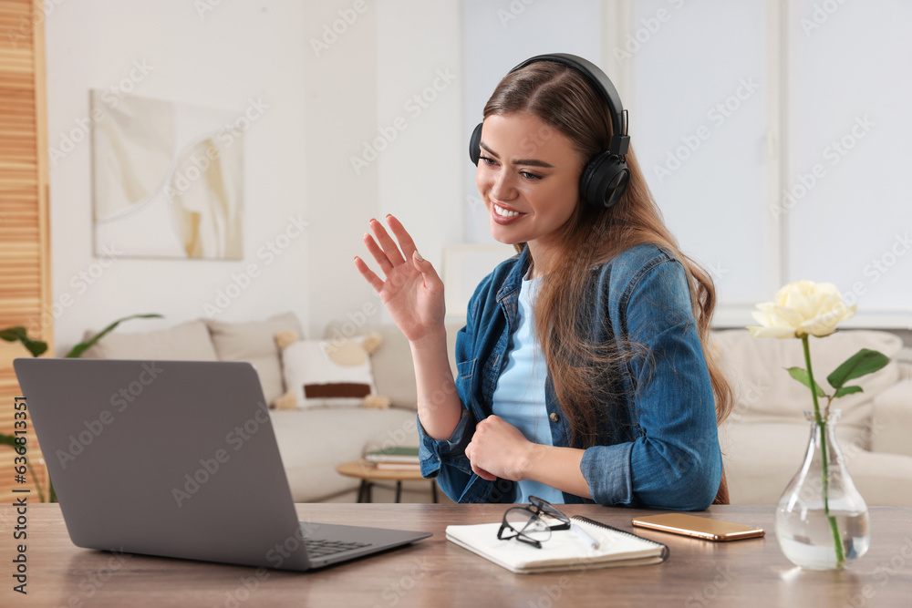 Happy woman with headphones having video chat via laptop at wooden table Happy woman with headphones having video chat via laptop at wooden table