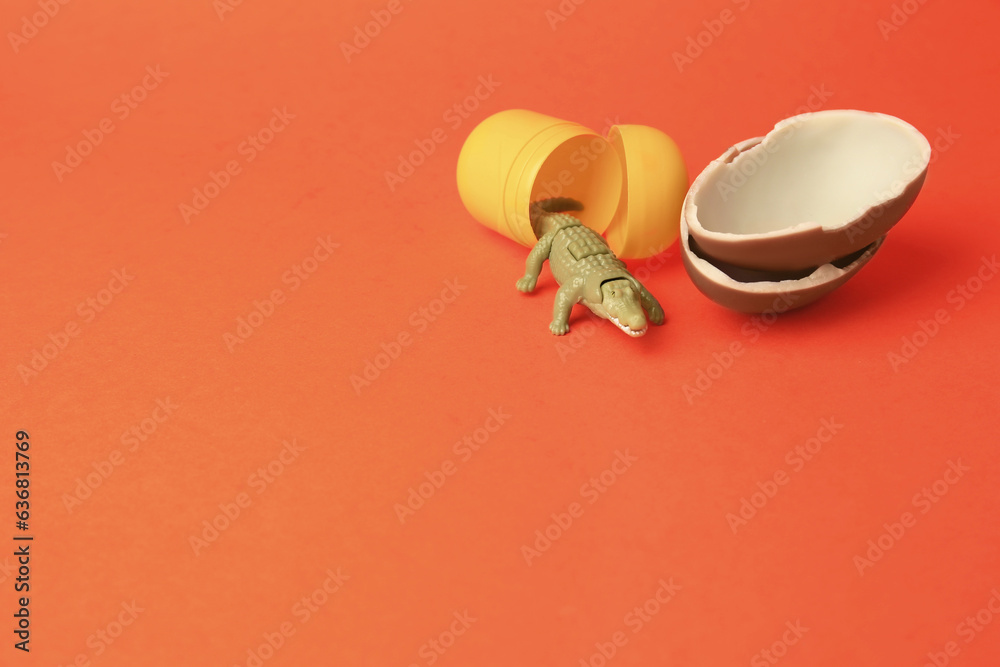 Slynchev Bryag, Bulgaria - May 25, 2023: Halves of Kinder Surprise Egg, plastic capsule and toy crocodile on orange background, space for text