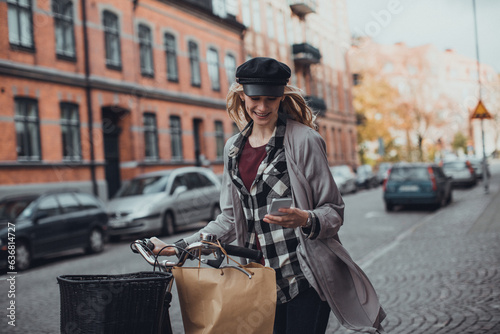 Young caucasian woman using a smart phone while pushing her bicycle on a city sidewalk
