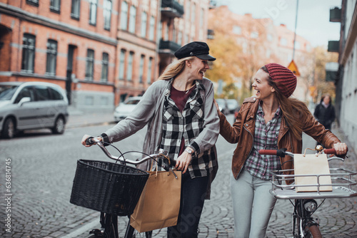 Young lesbian couple shopping and pushing their bicycles on a city street