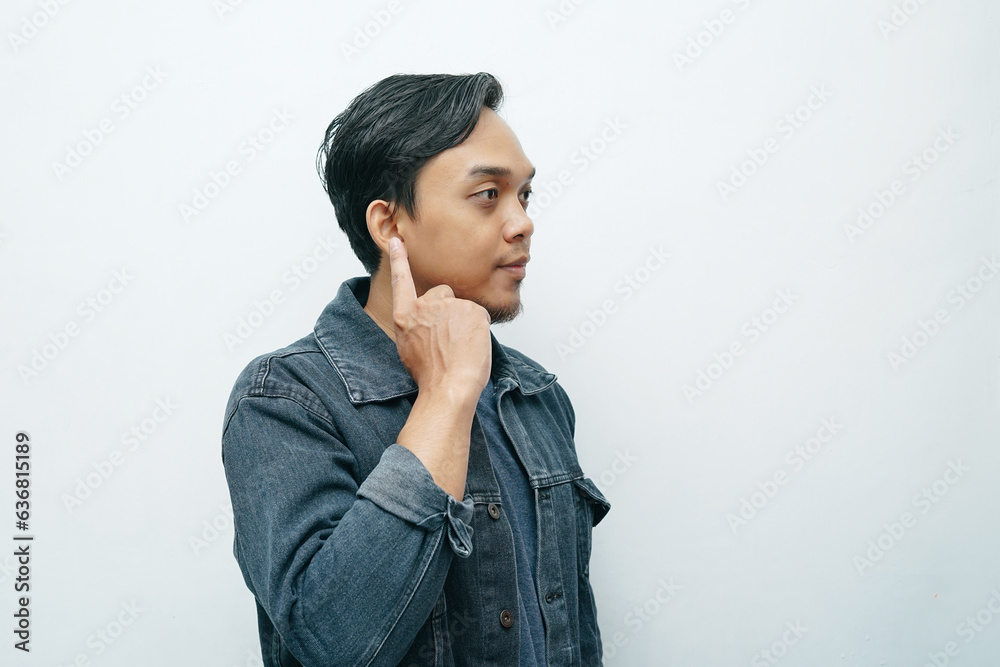 Portrait of Indonesian Asian man point his index finger on ear showing deafness gesture. Isolated white background Portrait of Indonesian Asian man point his index finger on ear showing deafness gesture. Isolated white background