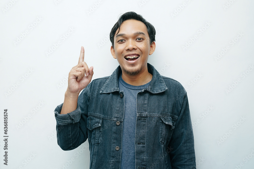 Portrait young Asian Indonesian man smiling and index finger pointing up with happy expression. Isolated white background Portrait young Asian Indonesian man smiling and index finger pointing up with happy expression. Isolated white background